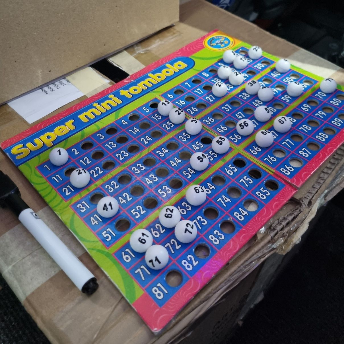 Bingo-Spielkarten mit weißen Kugeln auf blauen Feldern, Überschrift 'Super mini tombola' in Gelb und Rot auf grünem Hintergrund.