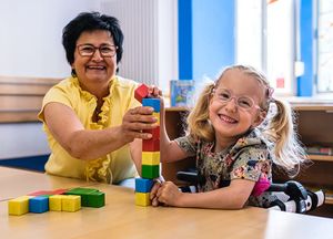 Eine Kita-Begleiterin baut mit einem Kind mit Bauklötzen. 