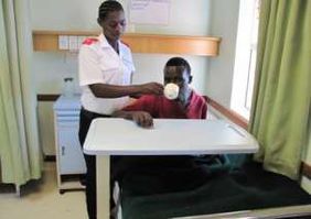 A nurse brings a patient a meal at the table.