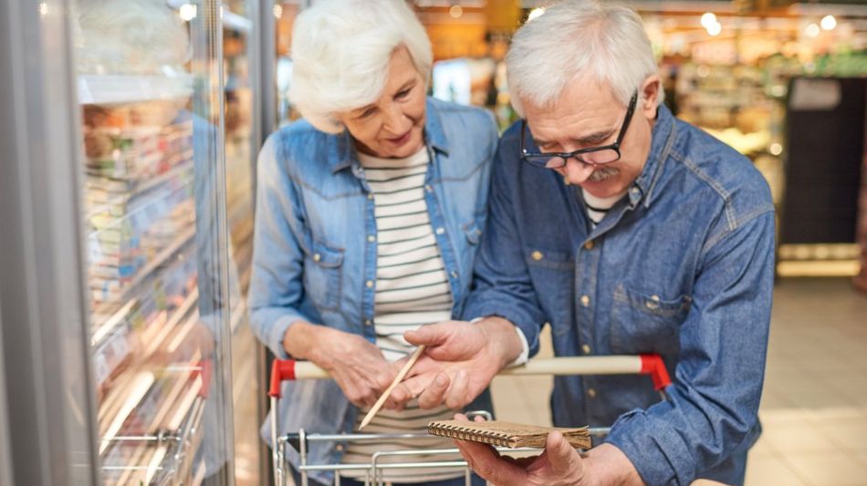 Ein älteres Paar mit Einkaufswagen und Einkaufsliste in einem Supermarkt.
