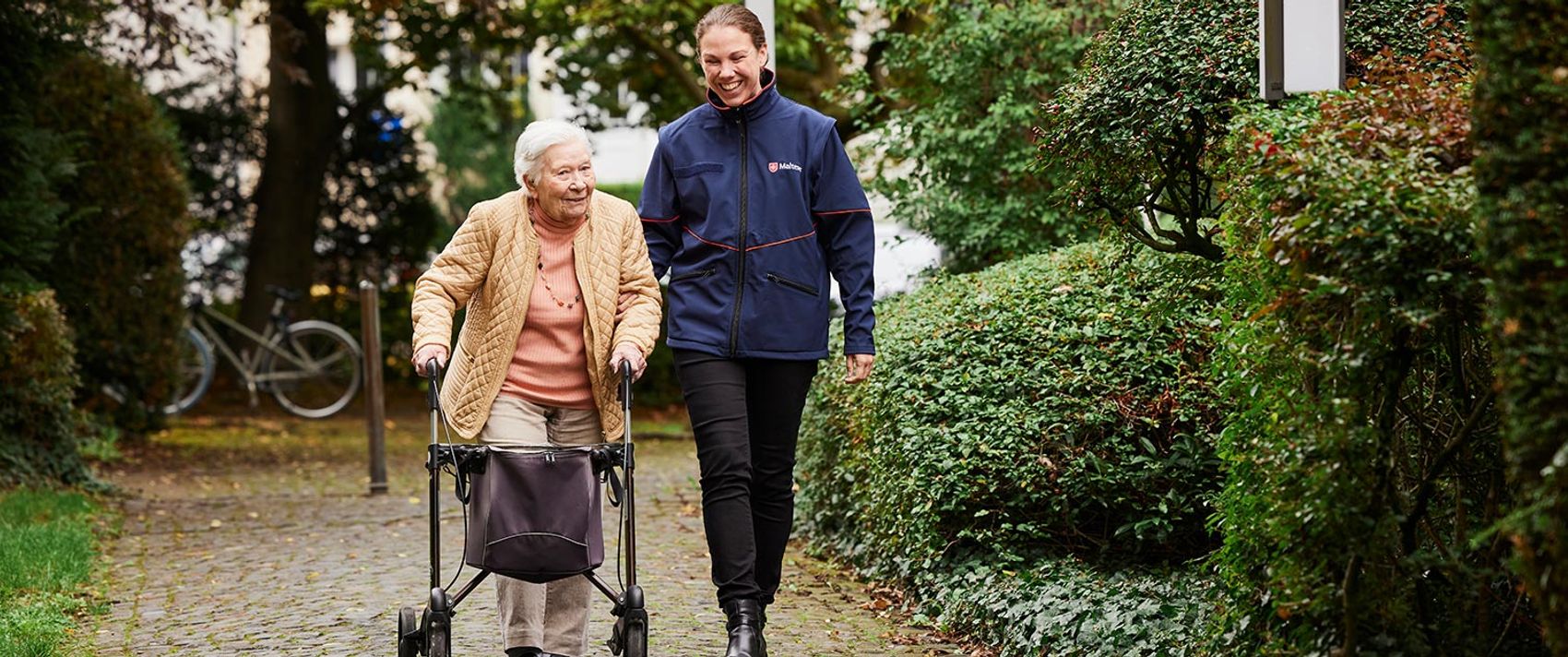 Eine Malteser Mitarbeiterin mit einer Seniorin im Park