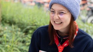 Junge Frau in Malteser Kleidung mit einer grauen Mütze sitzt im Freien an einer Schreibmaschine