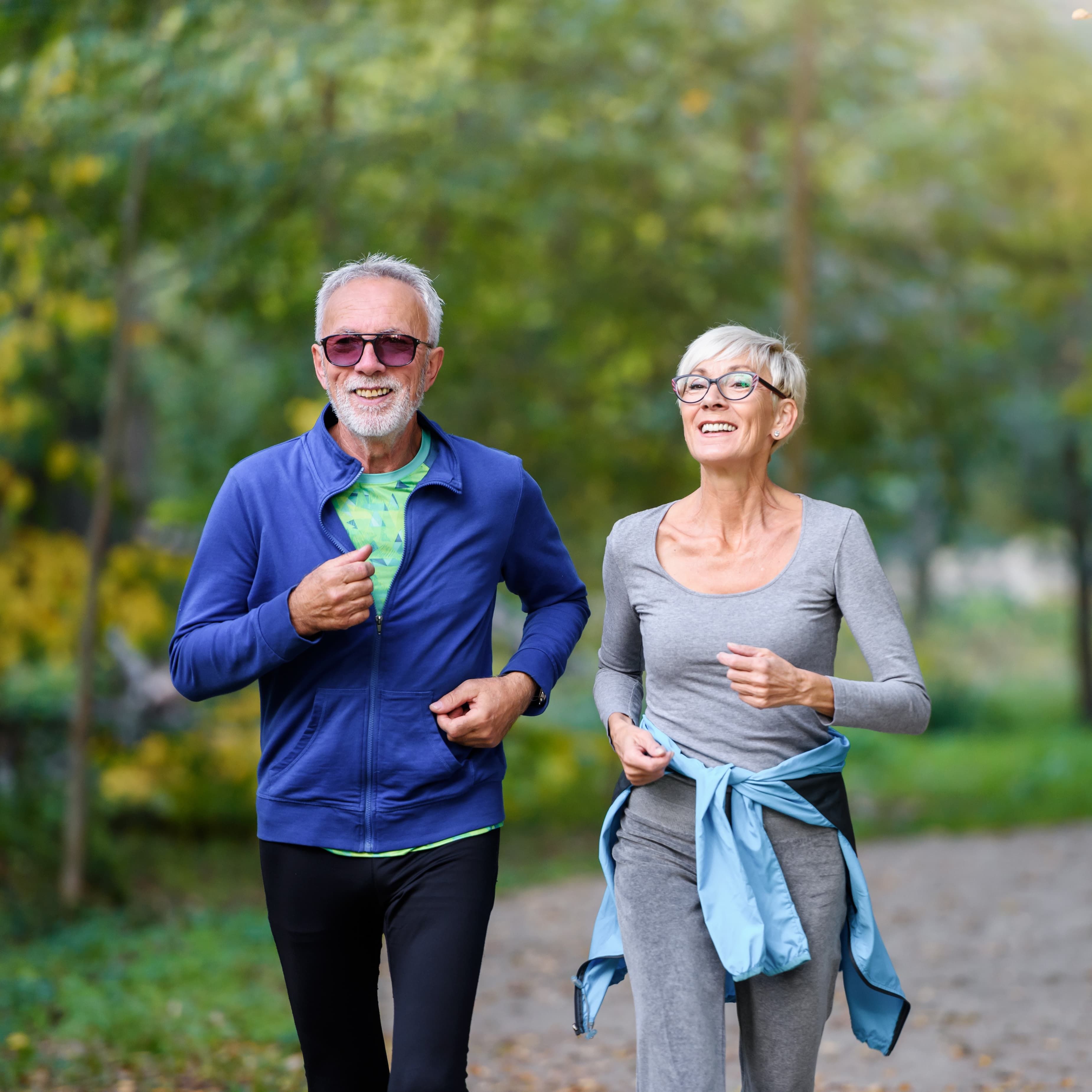 Zwei ältere Personen joggen gemeinsam auf einem Waldweg.