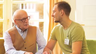 Man mit Malteser Namensschild sitzt neben älteren Herrn