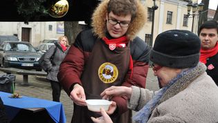 Ein Mitarbeiter des Malteser Auslandsdienstes versorgt eine ältere Frau mit einer warmen Mahlzeit.