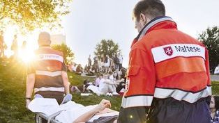 Zwei Sanitäter tragen eine verletzte Person über eine Wiese bei untergehenden Sonnen