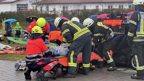 Einsatzkräfte von Maltesern und Feuerwehr lagern eine Verletztendarstellerin auf einer Rolltrage, im Hintergrund Publikum mit Regenschirmen.