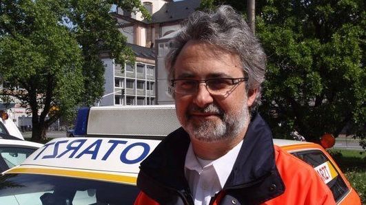 Porträtaufnahme von Dr. Rainer Löb vor einem Notarzt-Einsatzfahrzeug.