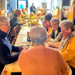 Menschen sitzen an einem Tisch. Sie sprechen miteinander.