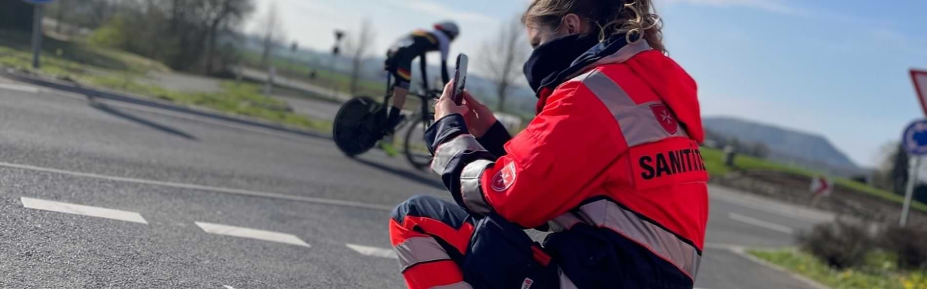 Eine Sanitäterin filmt ein Radrennen mit einem Smartphone.