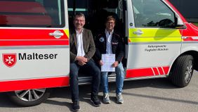 Zwei Männer sitzen bei geöffneter Seitentür in einem Malteser Rettungswagen.