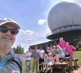 Die teilnehmenden des Ausflugs sitzen vor einer Bank an der Wasserkuppe. Foto: Malteser