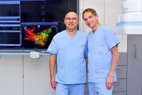 Zwei Männer in Arztkleidung vor einem Monitor.