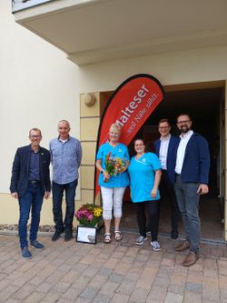 Sechs Personen stehen am Eingang des Pflegedienstes. Darunter Herr und Frau Scheuermann, der Bannewitzer Bürgermeister und zwei Malteser Vertreter. Im Hintergrund ist die Malteser Beachflag zu sehen.