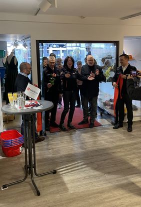 Die Ehrenamtlichen und ihre Gäste stehen im Eingang des Kleiderlädchens versammelt, das rote Band ist durchschnitten, Katharina Müller freut sich. Alle applaudieren. 