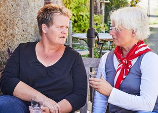 Zwei Frauen sitzen im Garten im Tisch und führen ein Gespräch. 