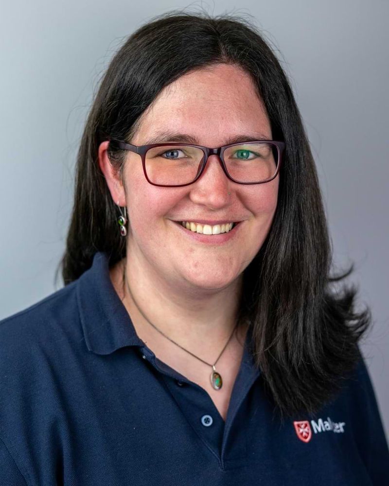 Portraitaufnahme einer lächelnden Frau in einem dunkelblauen Polohemd der Malteser. 