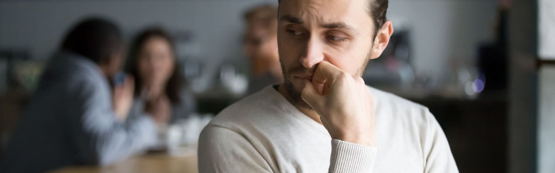 Ein junger Mann sitzt allein abseits von einer Menschengruppe