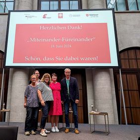 Mehrere Frauen und Männer haben sich vor einem Display aufgestellt.