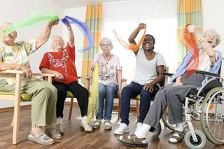 Fünf Frauen winken mit Tüchern und sitzen auf Stühlen.