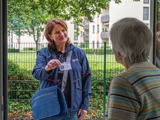 Ältere Dame öffnet die Haustür für die Mitarbeiterin der Malteser. 