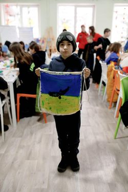Ein Junge hält einen selbstbemalten Jutebeutel mit der ukrainischen Flagge und Friedenstaube hoch.
