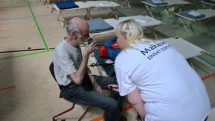 Eine Malteserin spricht mit einem Mann in einer Turnhalle voller Feldbetten