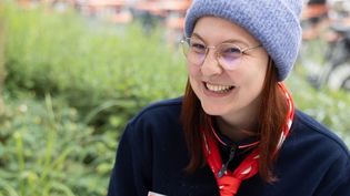 Junge Frau in Malteser Kleidung mit einer grauen Mütze sitzt im Freien an einer Schreibmaschine