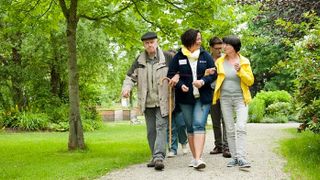 Eine Gruppe von 5 Menschen geht in einem Park spazieren. 