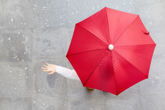 geöffneter roter Regenschirm, linke Hand schaut auf der Seite raus