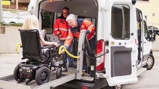 Zwei Mitarbeitende des Malteser Fahrdienstes helfen einer Frau im Rollstuhl ins Fahrzeug.