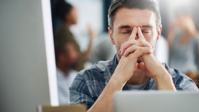 Junger Mann sitzt vor dem Computer und hält die Hände vor dem Kopf