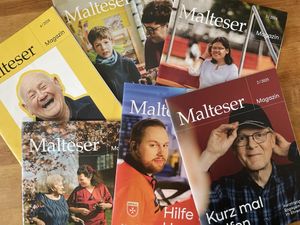 Sechs Ausgaben des „Malteser Magazin“ liegen überlappend auf Holz, mit verschiedenfarbigen Covern und teils unscharfen Personenfotos.