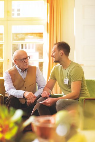 Man mit Malteser Namensschild sitzt neben älteren Herrn