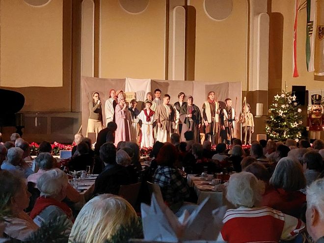 Viele sitzende Menschen lauschen einem Chor auf der Bühne.