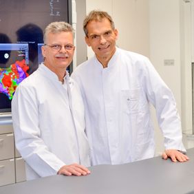 Zwei Ärzte in weißen Kitteln stehen nebeneinander in einem medizinischen Raum.