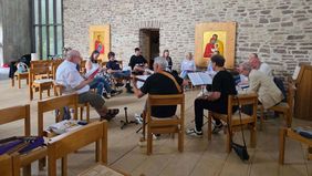Gruppe von Menschen sitzt auf Stühlen im Kreis und singt