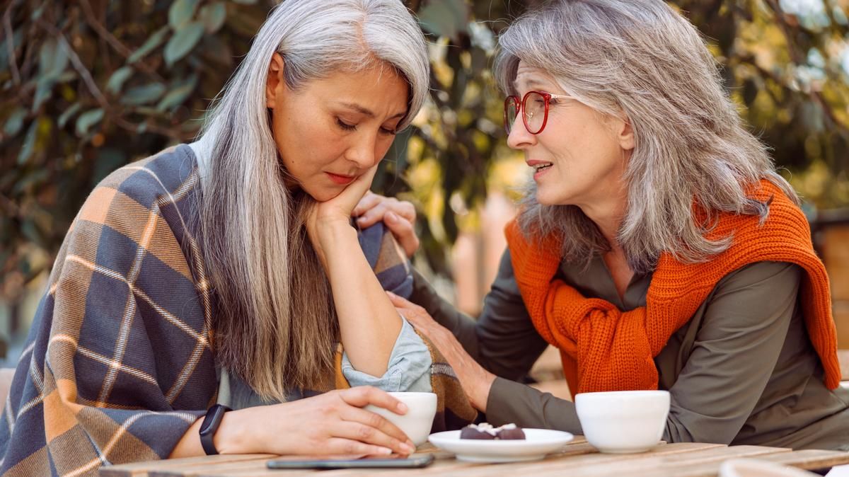 Zwei ältere Frauen unterhalten sich an einem kleinen Tisch im Außenbereich eines Cafés.