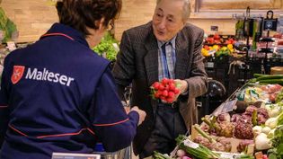 Malteser Helferin unterstützt einen älteren Mann beim Einkaufen im Supermarkt.