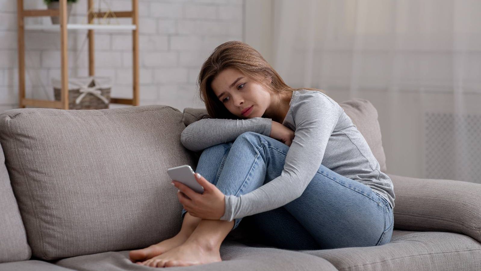Traurige Frau sitzt auf dem Sofa und schaut auf Ihr Smartphone