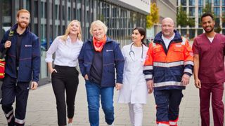 Malteser Mitarbeitende laufen gemeinsam durch den Innenhof eines Bürokomplexes.