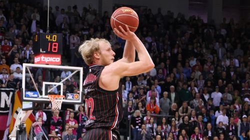 Spieler der Bamberg Baskets im schwarzen Trikot beim Sprungwurf, umgeben von einer vollen Zuschauertribüne.