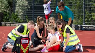 Malteser Schulsanitäter versorgen ein Mädchen, das sich beim Sport verletzt hat.