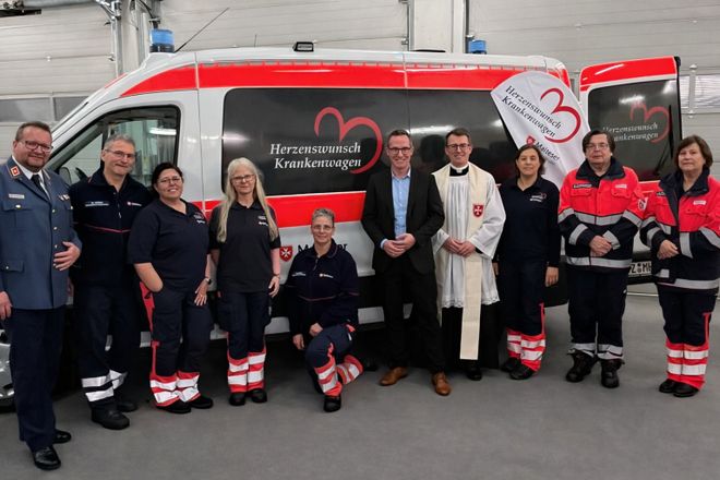 Viele Malteser in Dienstkleidung stehen neben Landrat Carsten Braun vor dem neuen Herzenswunschkrankenwagen