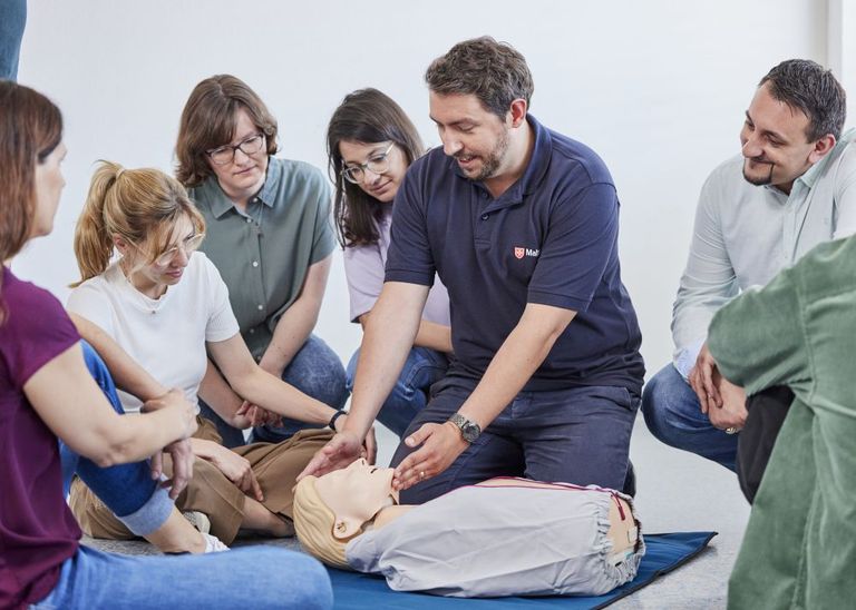 Ein Ausbilder zeigt einer Gruppe an einer Übungspuppe das Überstrecken des Kopfes.