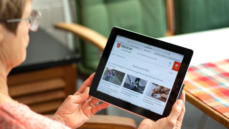 Älter Frau hält ein Tablett in den Händen und schaut auf den Bildschirm.