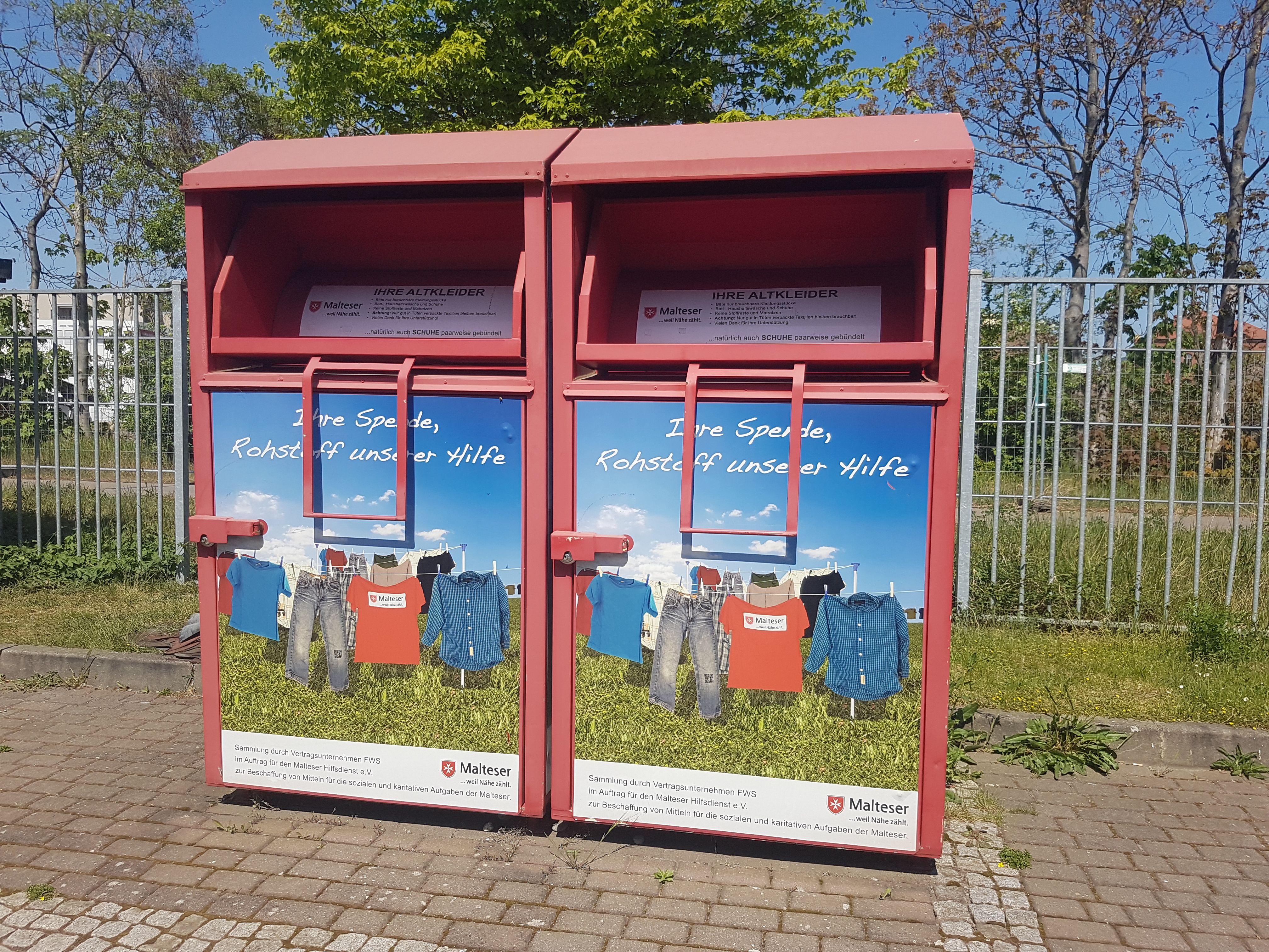 Zwei Altkleidercontainer der Malteser stehen auf einem Weg.