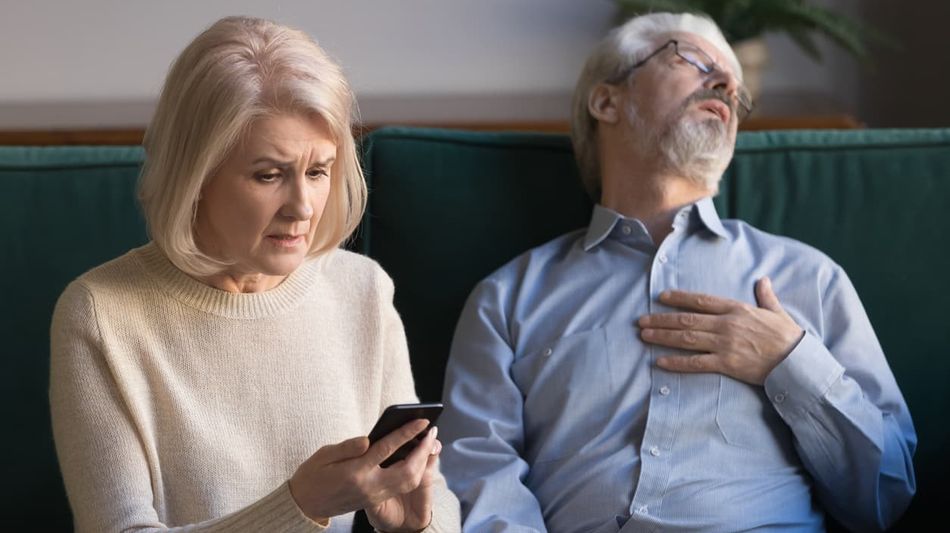 Neben einer Frau mit Handy in der Hand sitzt ohnmächtig ein älterer Mann und fasst sich ans Herz