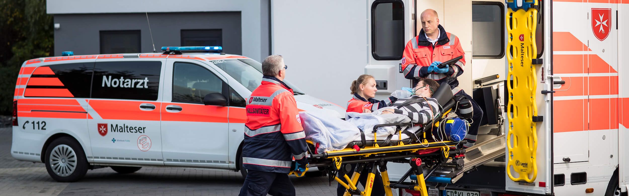 Drei Rettungsdienstsanitäter schieben Trage mit Patienten in den Rettungswagen