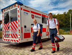 Zwei junge Sanitäter mit Notfallrucksäcken haben den Rettungswagen verlassen und sind bereit für den Einsatz.